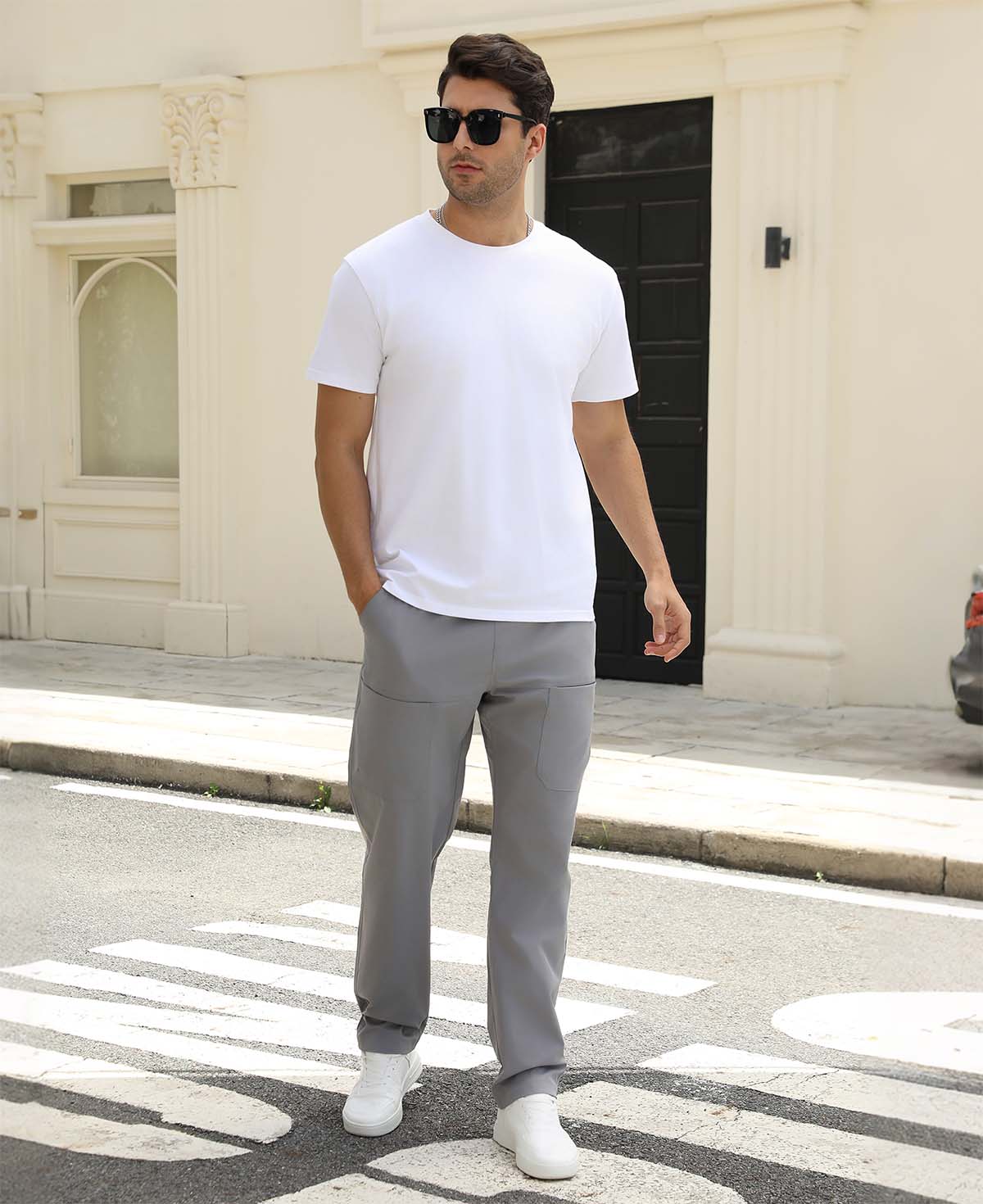 Man wearing white tee and light grey durable multipants standing on a street, hand in pocket, showcasing daily wear.
