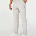 Man in white multipants with drawstring waist and multiple pockets, white sneakers, hand in pocket showing side logo.