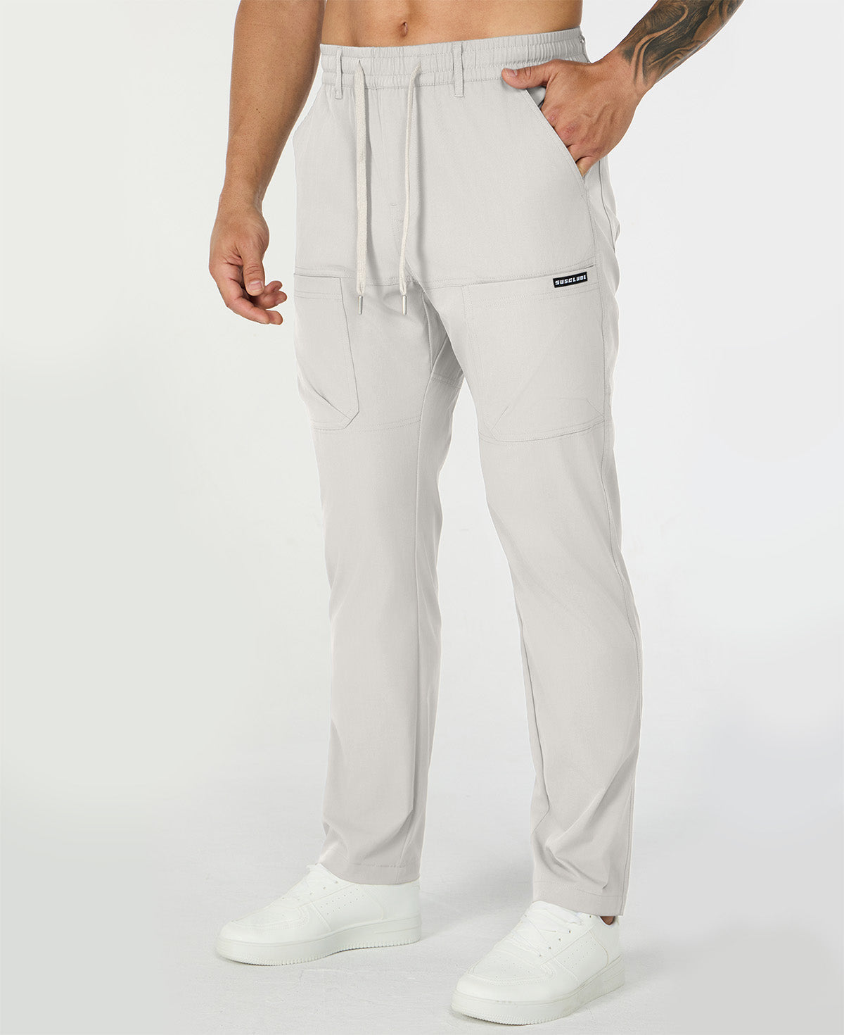 Man in white multipants with drawstring waist and multiple pockets, white sneakers, hand in pocket showing side logo.