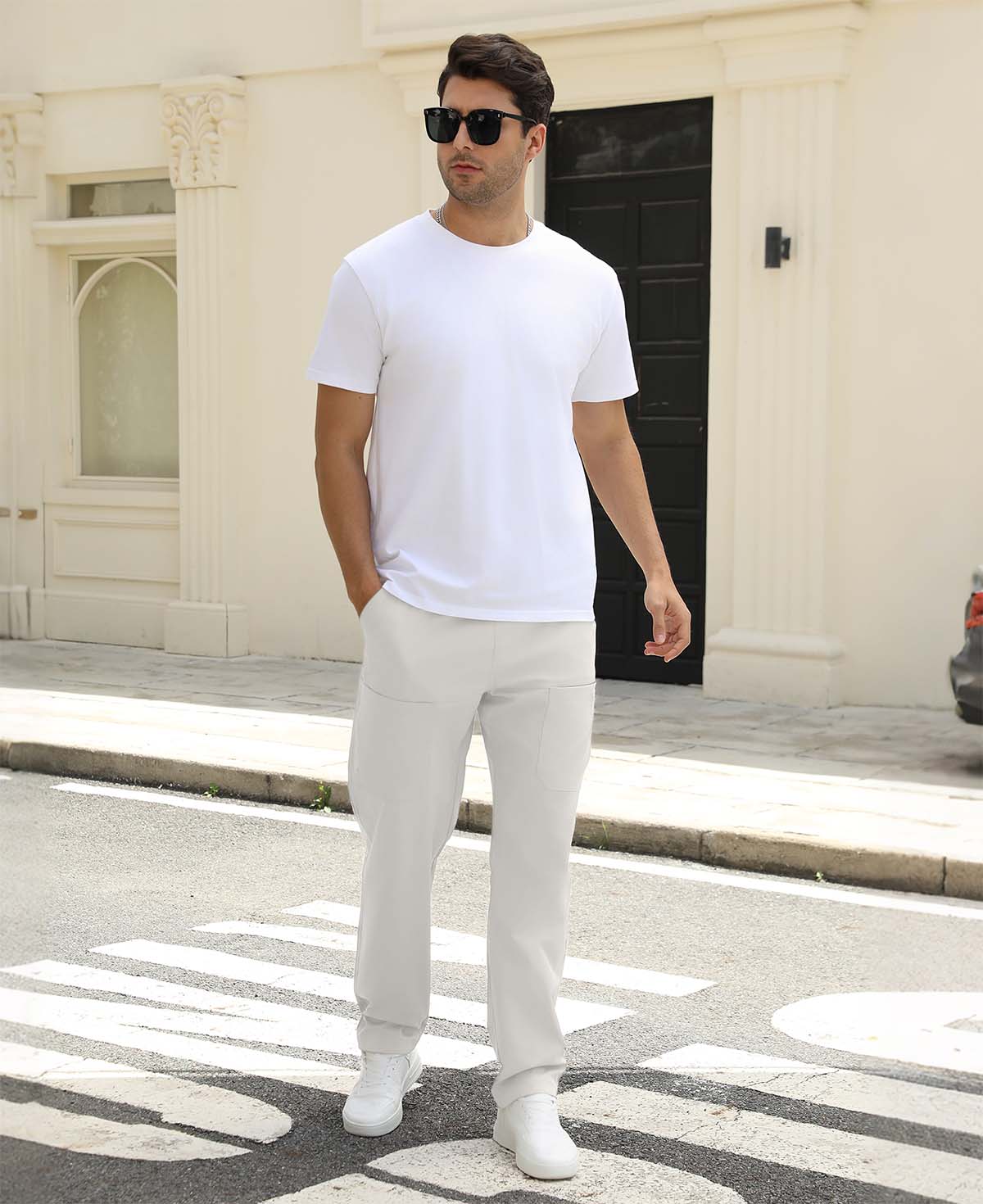 Man wearing white tee and white durable multipants standing on a street, hand in pocket, showcasing daily wear.