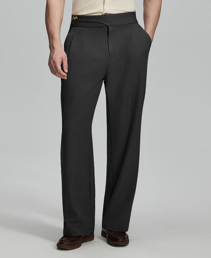 Man in beige sweater, black Gurkha pants & brown shoes, hand in pocket showing pleated wide leg drape and flow.