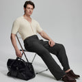 Model in beige knit and black Gurkha trousers with black bag, leaning on chair, elegant smart-casual look.