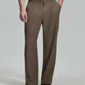 Man in beige sweater, brown Gurkha pants & brown shoes, hand in pocket showing pleated wide leg drape and flow.