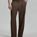 Man in beige sweater, brown Gurkha pants & brown shoes, hand in pocket showing pleated wide leg drape and flow.