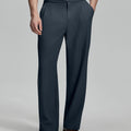 Man in beige sweater, grey Gurkha pants & brown shoes, hand in pocket showing pleated wide leg drape and flow.