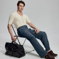 Model in beige knit and grey Gurkha trousers with black bag, leaning on chair, elegant smart-casual look.
