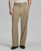 Man in beige sweater, beige Gurkha pants & brown shoes, hand in pocket showing pleated wide leg drape and flow.