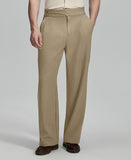 Man in beige sweater, beige Gurkha pants & brown shoes, hand in pocket showing pleated wide leg drape and flow.
