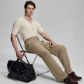 Model in beige knit and beige Gurkha trousers with black bag, leaning on chair, elegant smart-casual look.