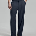 Man in beige sweater, navy Gurkha pants & brown shoes, hand in pocket showing pleated wide leg drape and flow.