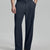 Man in beige sweater, navy Gurkha pants & brown shoes, hand in pocket showing pleated wide leg drape and flow.