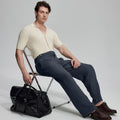 Model in beige knit and navy Gurkha trousers with black bag, leaning on chair, elegant smart-casual look.