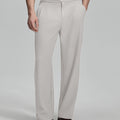 Man in beige sweater, grey Gurkha pants & brown shoes, hand in pocket showing pleated wide leg drape and flow.