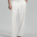 Man in beige sweater, white Gurkha pants & brown shoes, hand in pocket showing pleated wide leg drape and flow.