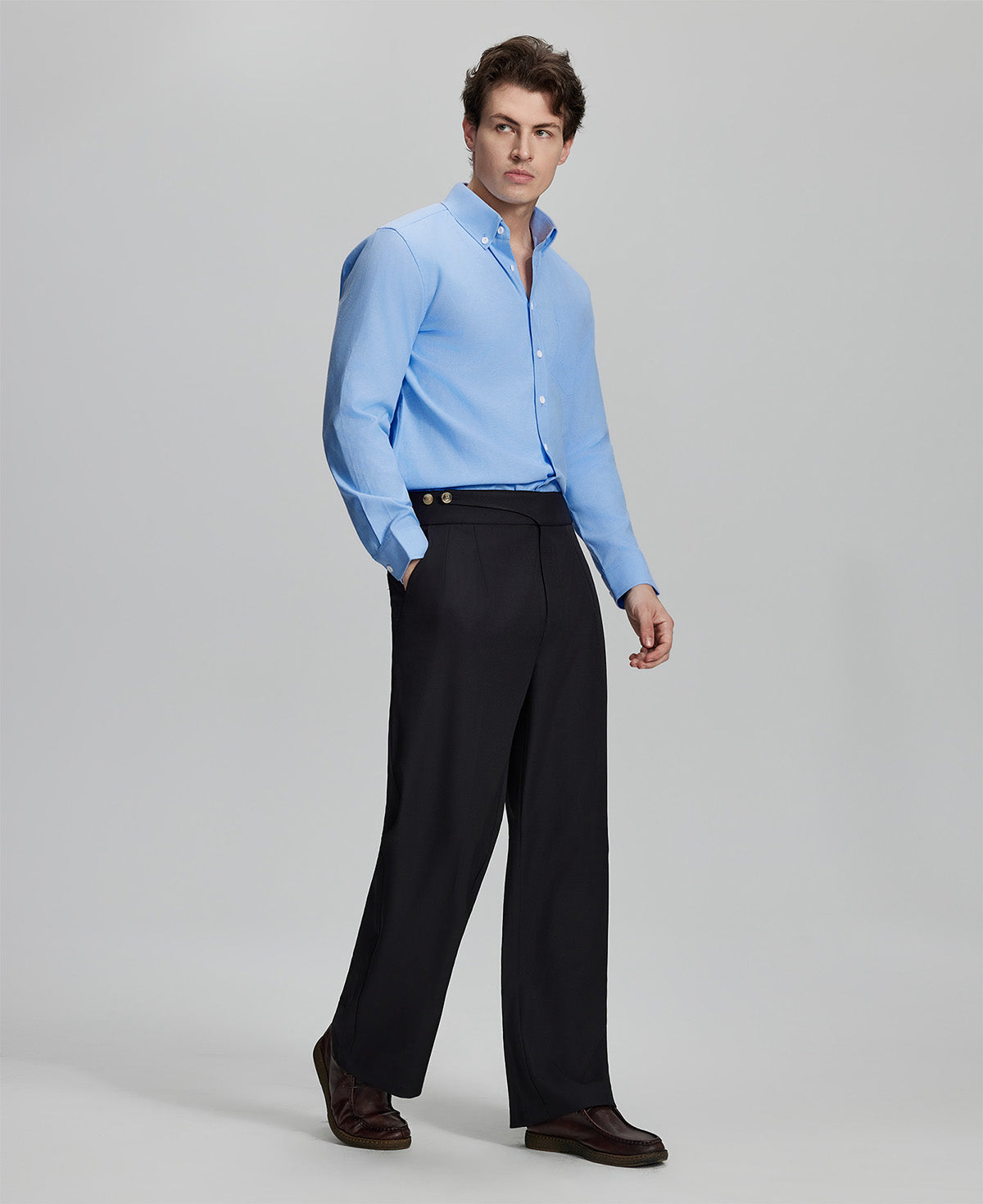 Side profile of model in light blue Oxford shirt and trousers, clean lines and sharp silhouette.