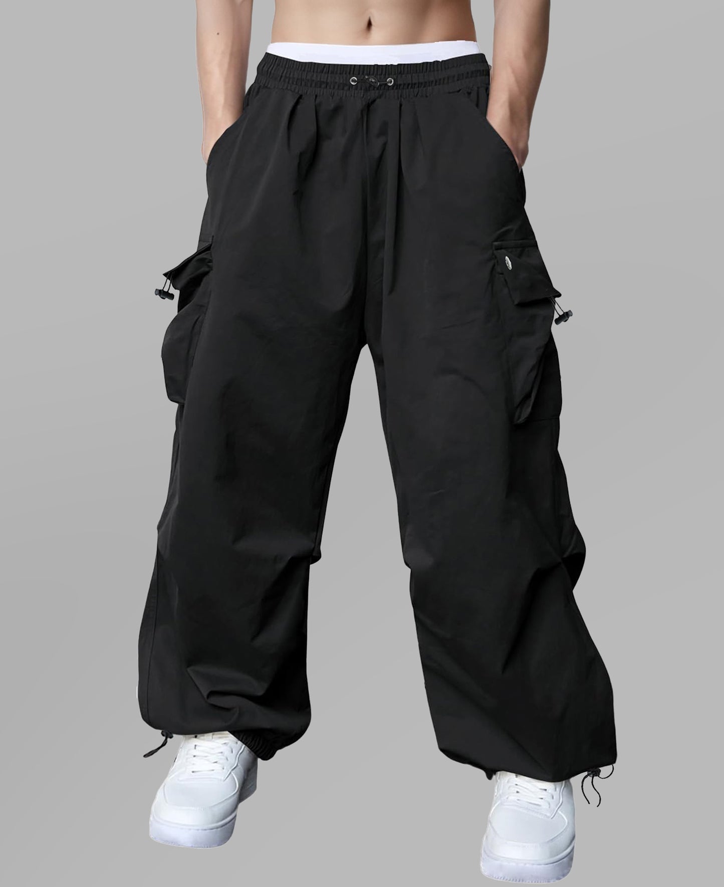 Man in black baggy sweatpants, high waist, five pockets, back logo. White sneakers, standing front.