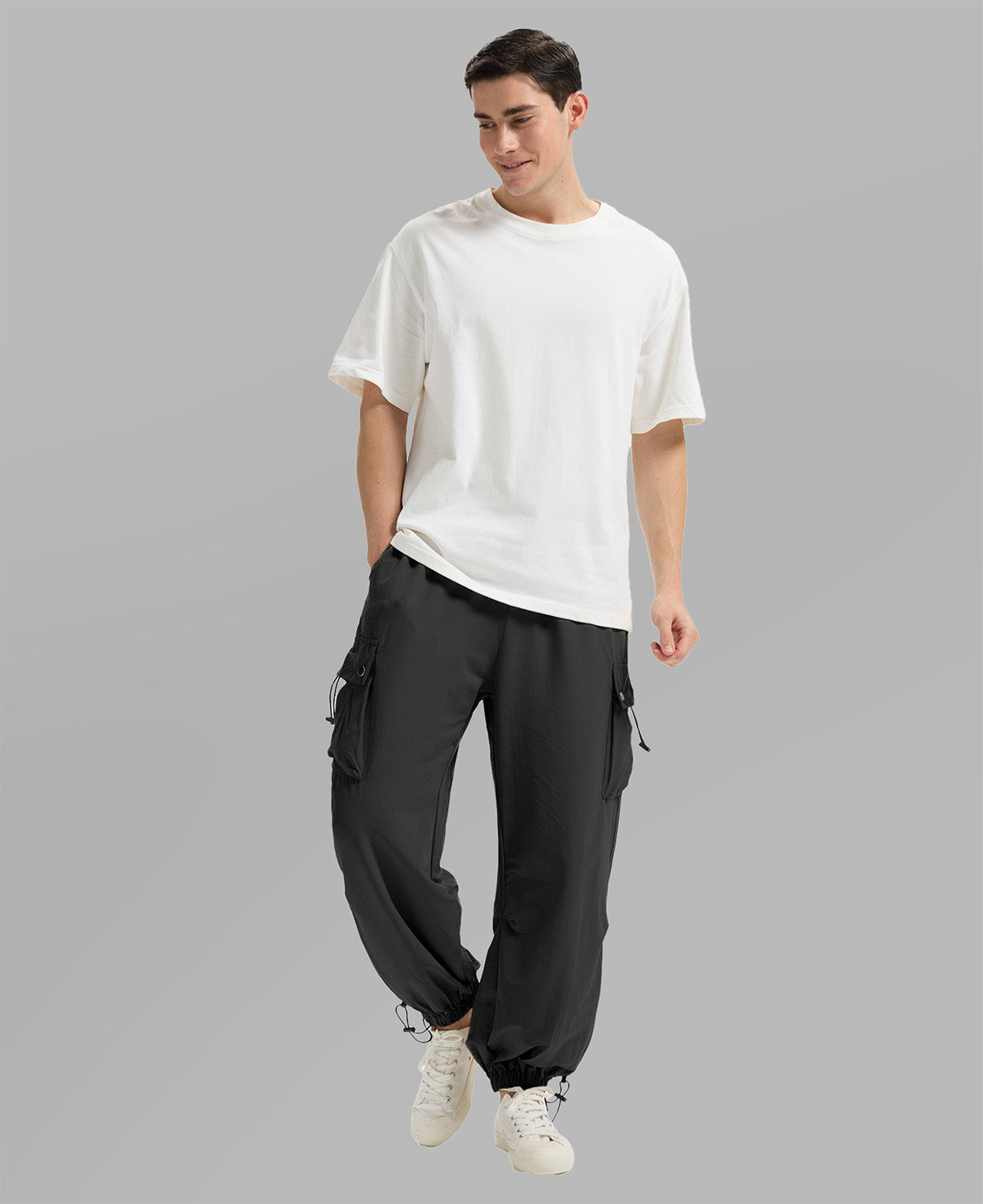 Full view of man wearing black baggy sweatpants with white tee and sneakers, highlighting fit.