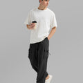 Side view of man in black baggy sweatpants holding coffee cup, showing side pocket details.