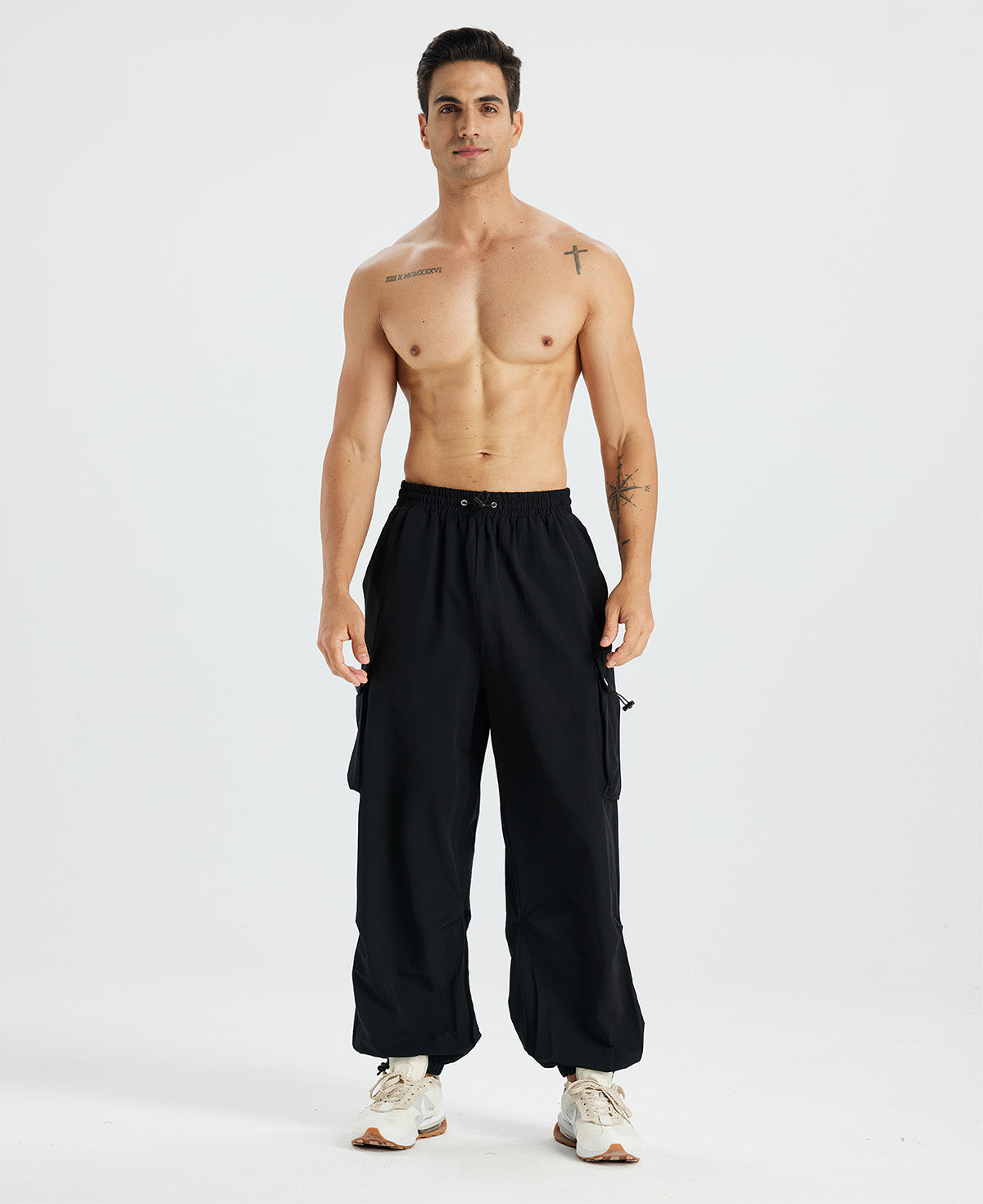 Bare-chested man in black baggy sweatpants, white shoes, highlighting waist and length details.