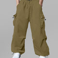 Man in brown baggy sweatpants, high waist, five pockets, back logo. White sneakers, standing front.