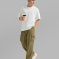 Side view of man in brown baggy sweatpants holding coffee cup, showing side pocket details.