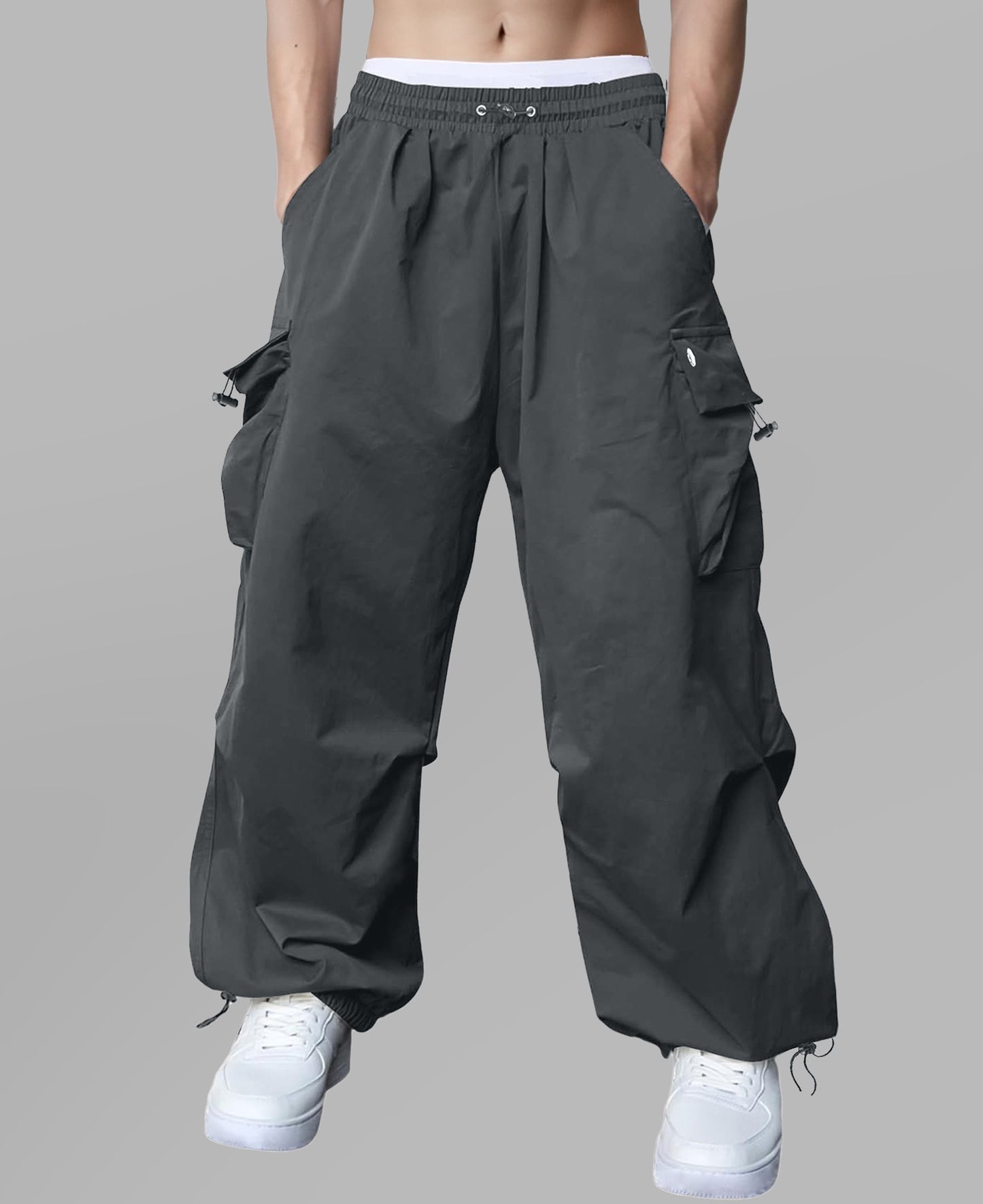Man in dark grey baggy sweatpants, high waist, five pockets, back logo. White sneakers, standing front.
