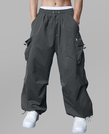 Man in dark grey baggy sweatpants, high waist, five pockets, back logo. White sneakers, standing front.