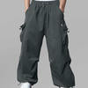 Man in dark grey baggy sweatpants, high waist, five pockets, back logo. White sneakers, standing front.