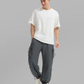 Full view of man wearing dark grey baggy sweatpants with white tee and sneakers, highlighting fit.