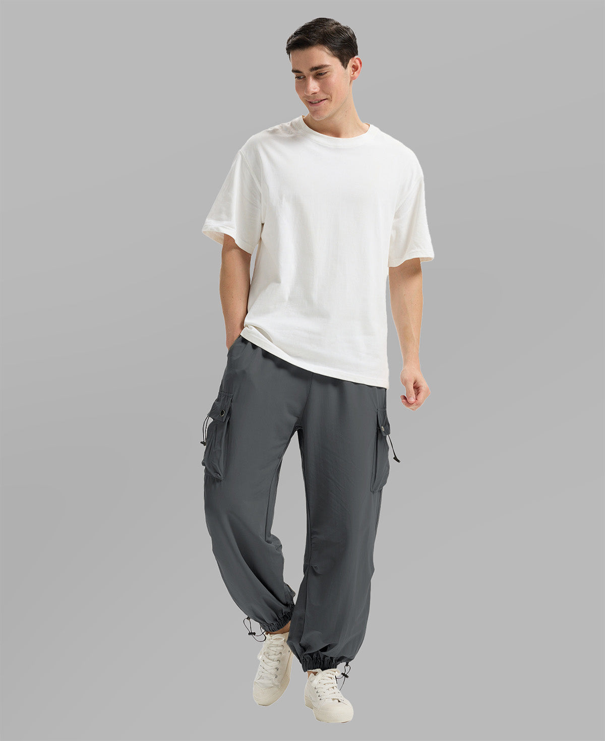 Full view of man wearing dark grey baggy sweatpants with white tee and sneakers, highlighting fit.