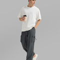 Side view of man in dark grey baggy sweatpants holding coffee cup, showing side pocket details.