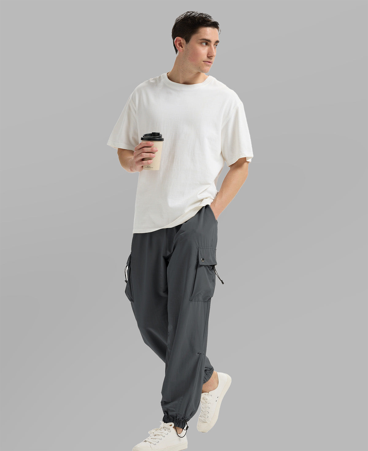 Side view of man in dark grey baggy sweatpants holding coffee cup, showing side pocket details.
