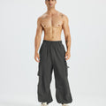 Bare-chested man in dark grey baggy sweatpants, white shoes, highlighting waist and length details.