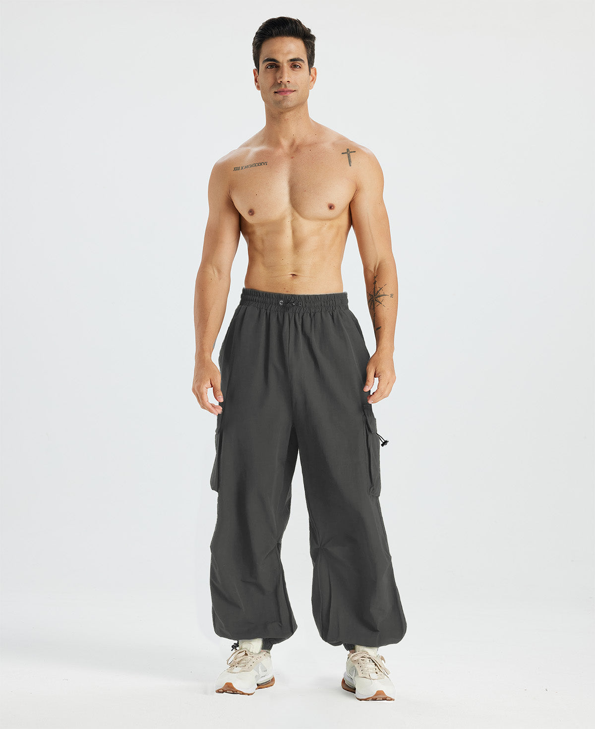 Bare-chested man in dark grey baggy sweatpants, white shoes, highlighting waist and length details.