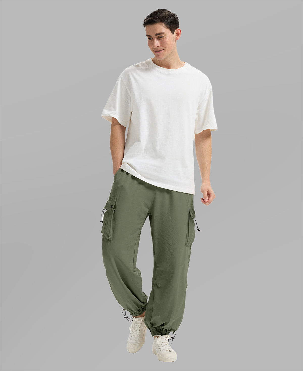 Full view of man wearing light green baggy sweatpants with white tee and sneakers, highlighting fit.
