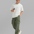 Side view of man in light green baggy sweatpants holding coffee cup, showing side pocket details.