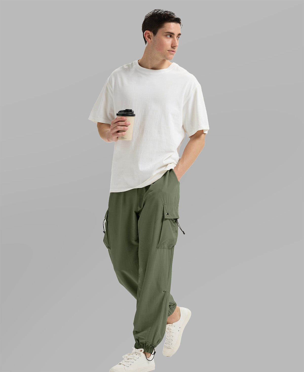 Side view of man in light green baggy sweatpants holding coffee cup, showing side pocket details.