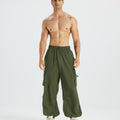 Bare-chested man in light green baggy sweatpants, white shoes, highlighting waist and length details.