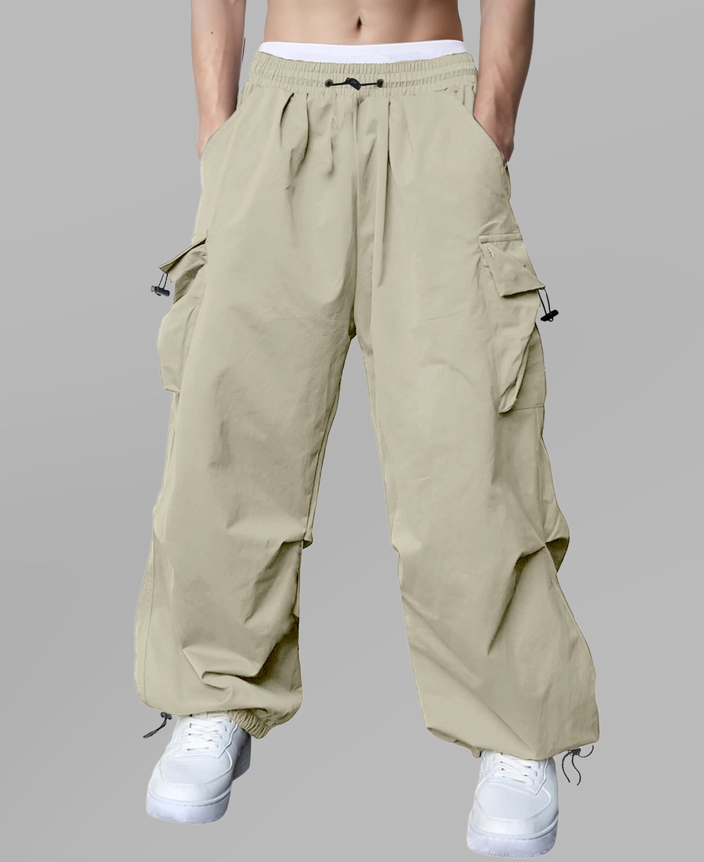 Man in khaki baggy sweatpants, high waist, five pockets, back logo. White sneakers, standing front.