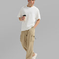 Side view of man in khaki baggy sweatpants holding coffee cup, showing side pocket details.