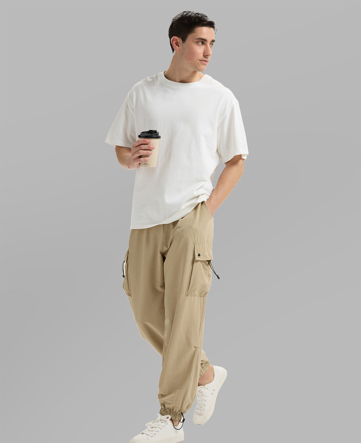 Side view of man in khaki baggy sweatpants holding coffee cup, showing side pocket details.