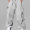 Man in light grey baggy sweatpants, high waist, five pockets, back logo. White sneakers, standing front.