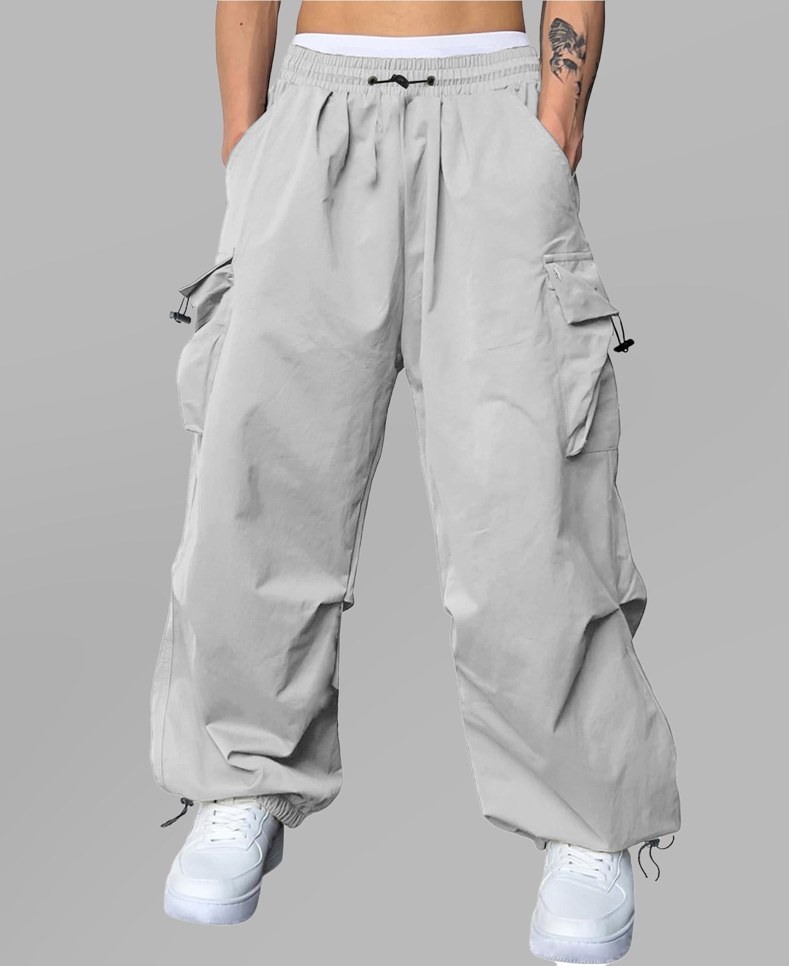 Man in light grey baggy sweatpants, high waist, five pockets, back logo. White sneakers, standing front.