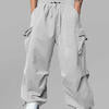 Man in light grey baggy sweatpants, high waist, five pockets, back logo. White sneakers, standing front.