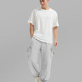 Full view of man wearing light grey baggy sweatpants with white tee and sneakers, highlighting fit.