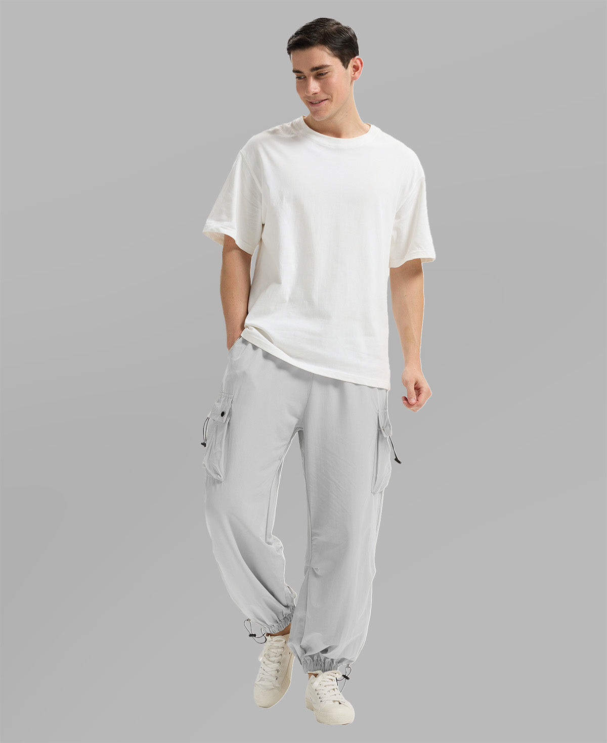 Full view of man wearing light grey baggy sweatpants with white tee and sneakers, highlighting fit.