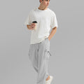 Side view of man in light grey baggy sweatpants holding coffee cup, showing side pocket details.