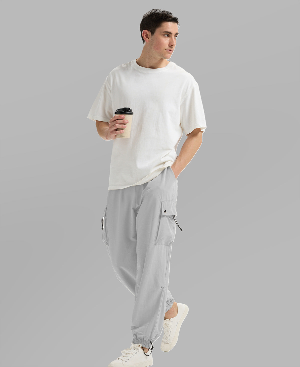 Side view of man in light grey baggy sweatpants holding coffee cup, showing side pocket details.
