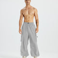Bare-chested man in light grey baggy sweatpants, white shoes, highlighting waist and length details.