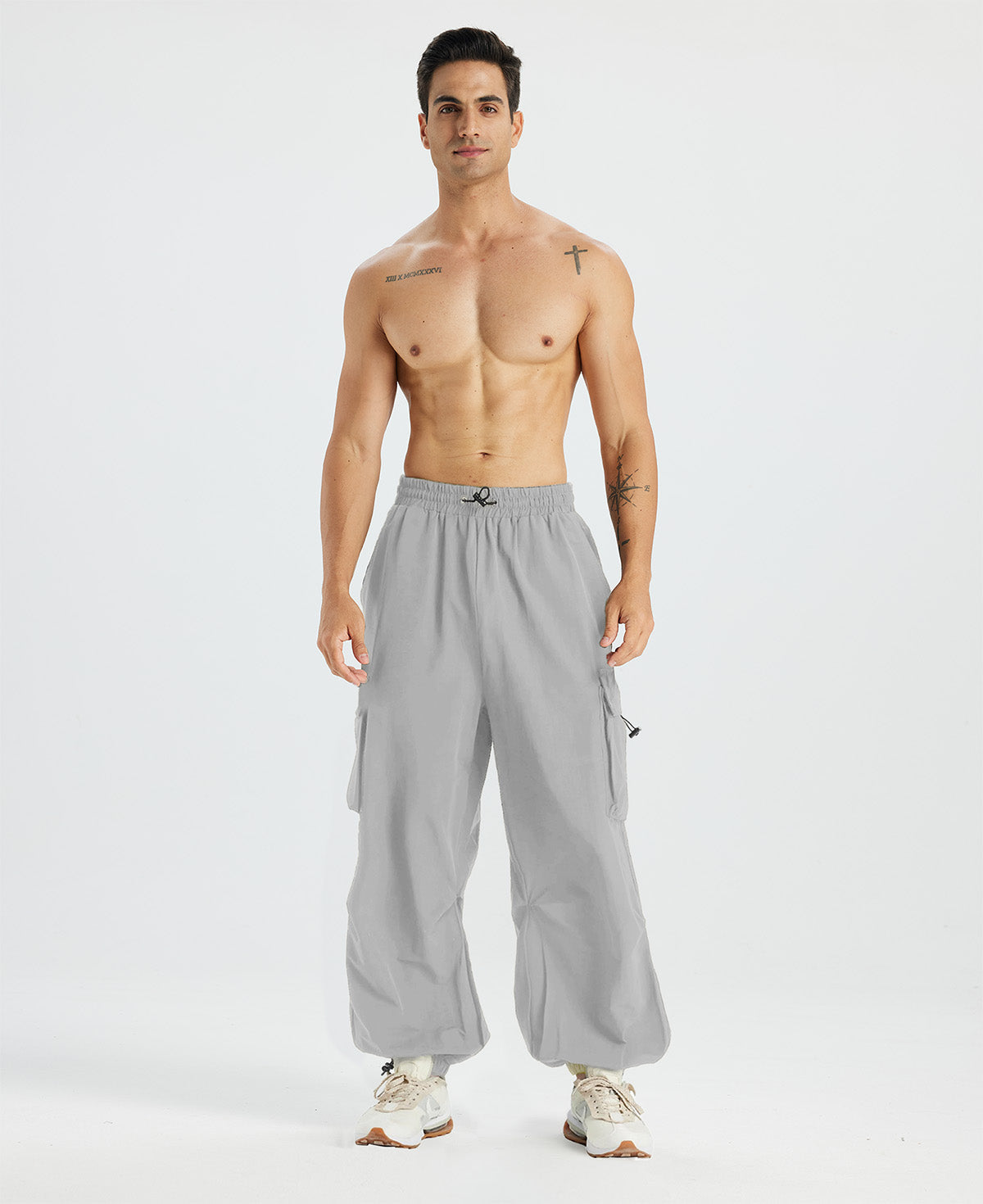 Bare-chested man in light grey baggy sweatpants, white shoes, highlighting waist and length details.